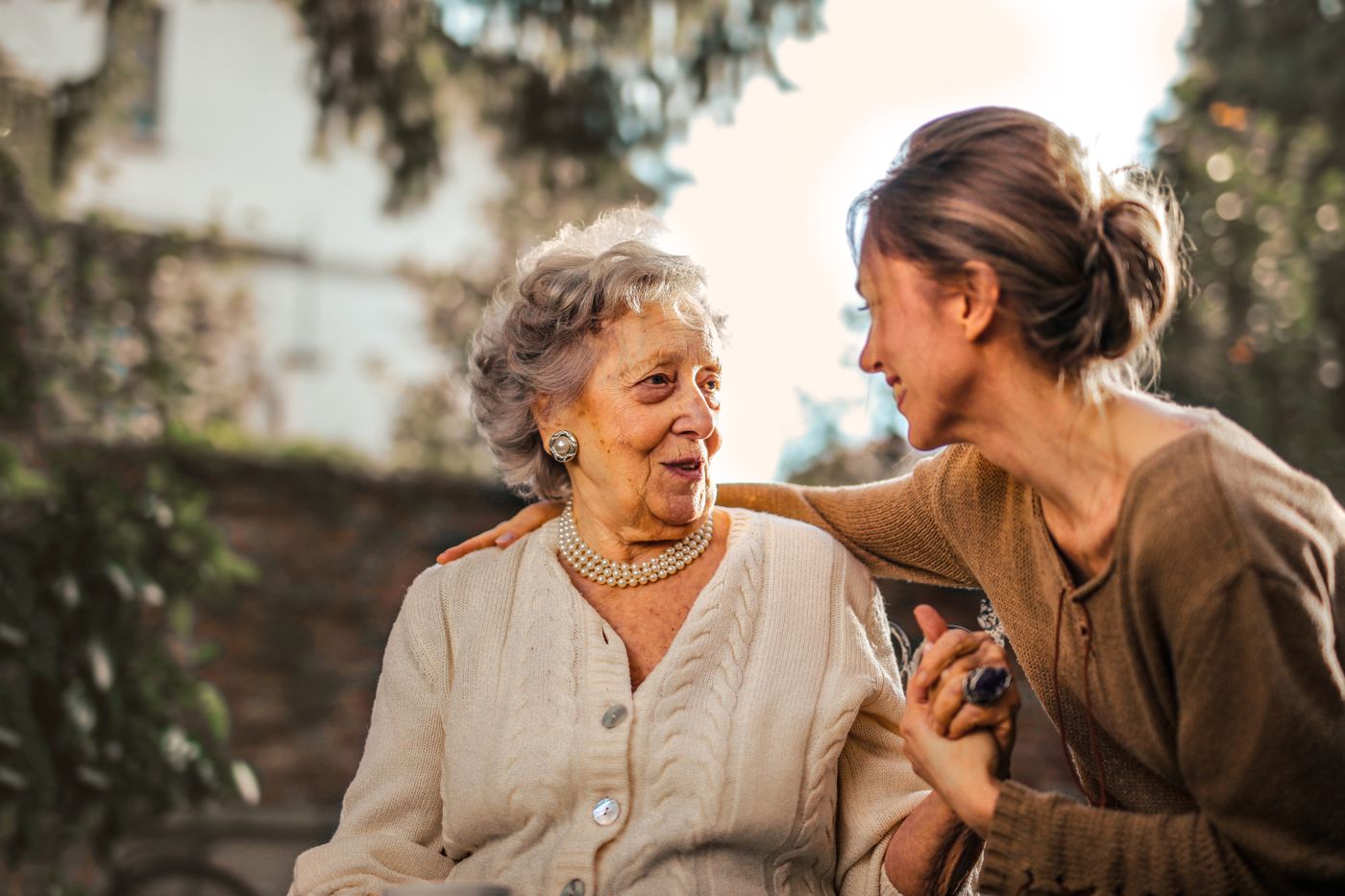 A family member sitting with an older parent, holding her hand and talking together.