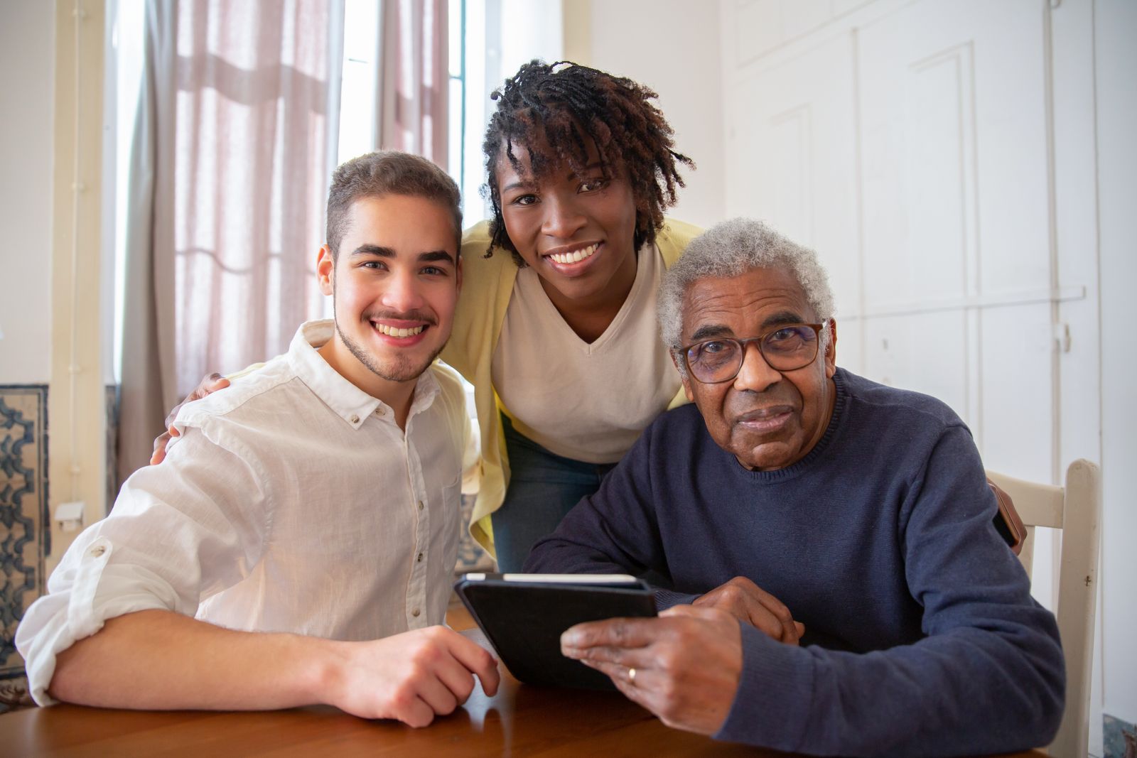 A caregiver sitting with an older adult at a table in a bright home.