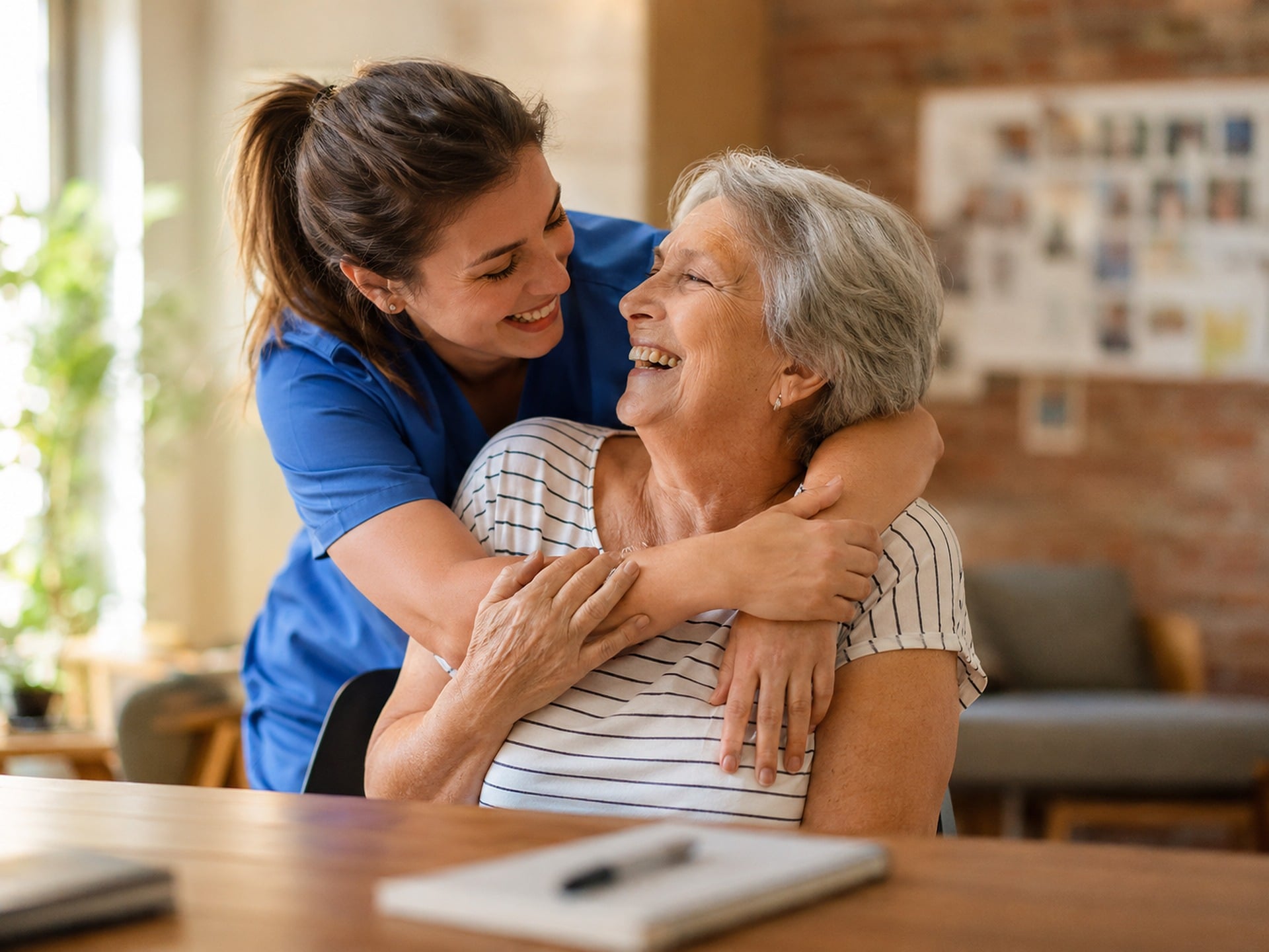 A caregiver sitting with an older adult at a table in a bright home.